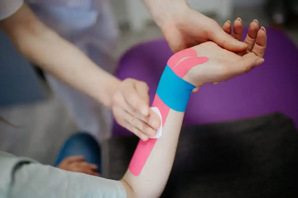Close-up of kinesio tape application on a person's forearm by a therapist for therapeutic support and pain management.